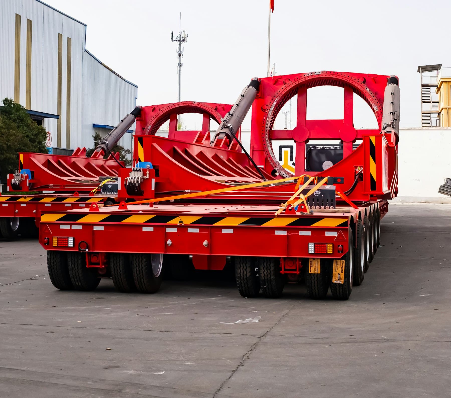 Multi-axle heavy-haul trailers fitted with red wind-turbine blade root adapters