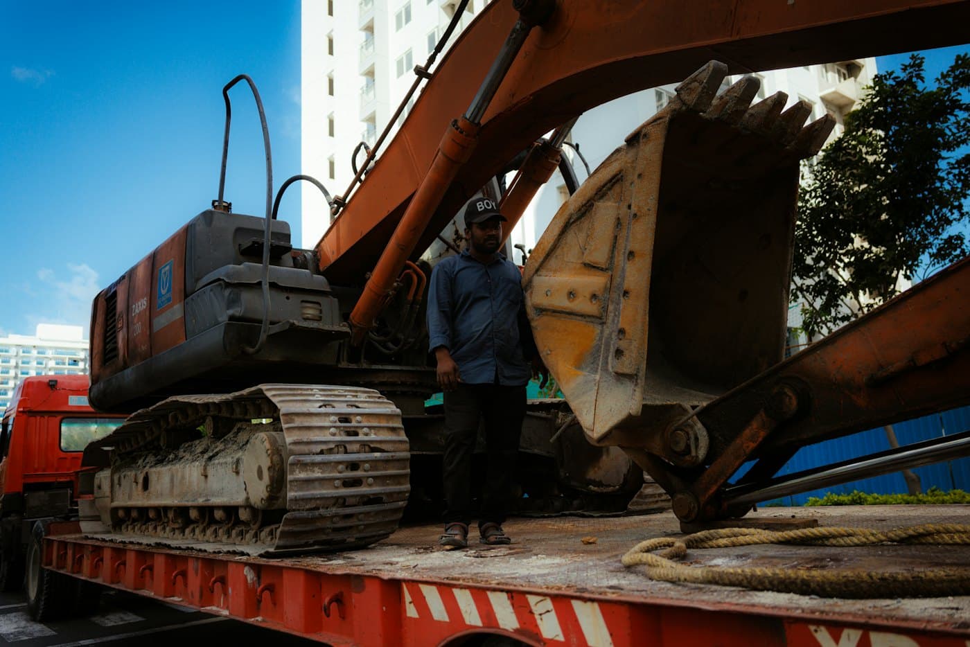 A crew member alongside tracked plant secured on a low-bed trailer